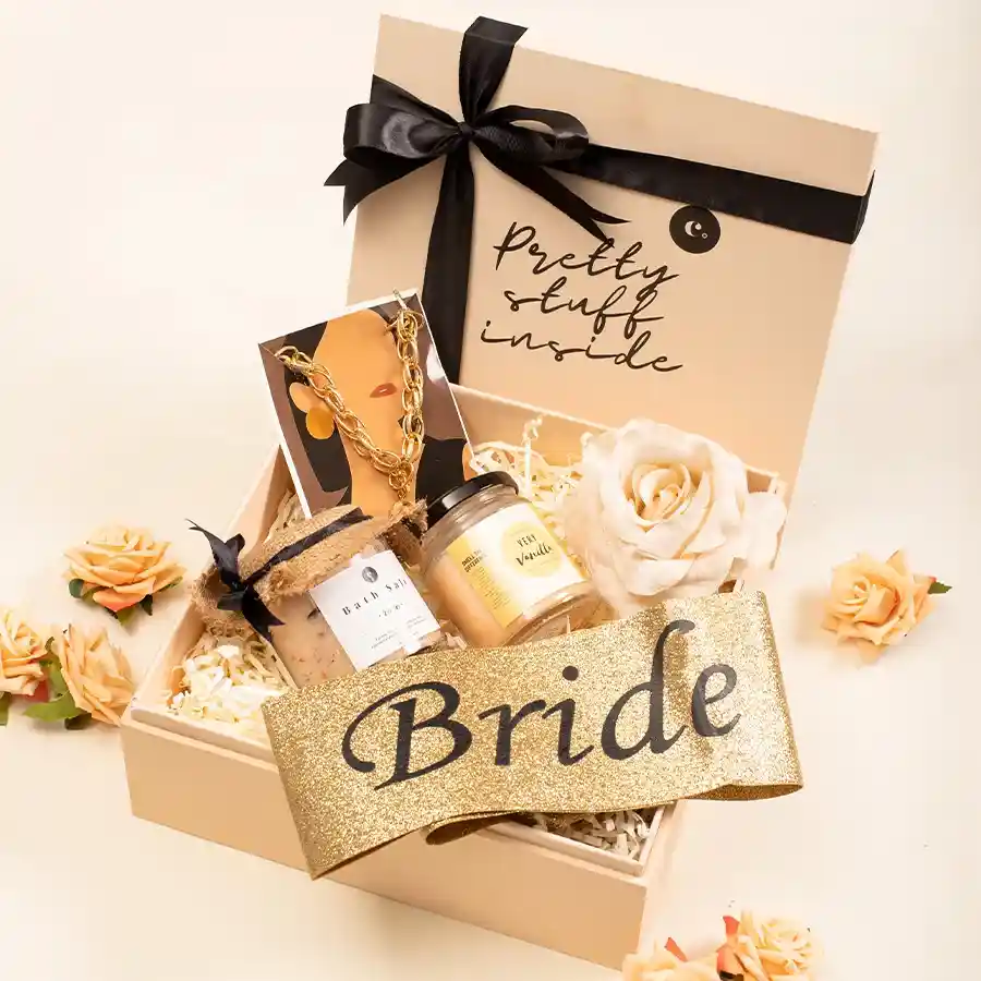 Bridal Bliss Celebration Hamper featuring a golden necklace, bride sash, vanilla scented candle, rose bath salt, and a reusable decorative box.