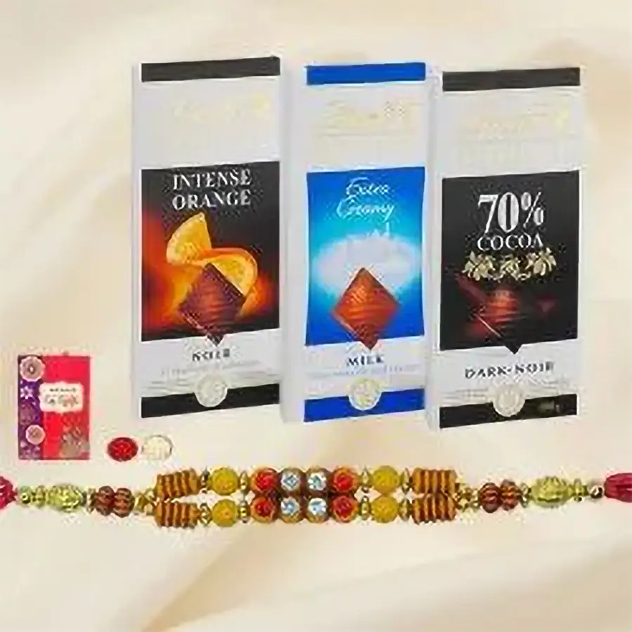 An assortment of Lindt chocolate bars including Extra Creamy, Orange Intense, and Excellence 70, alongside two Rakhis and Roli Tilak Chawal sets on a decorative background.