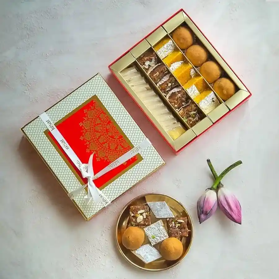 Kesar Sweet Symphony Gift Box with assorted Indian sweets including Besan Laddoo, Kaju Katli, Moong Thal, and Doda Burfi.