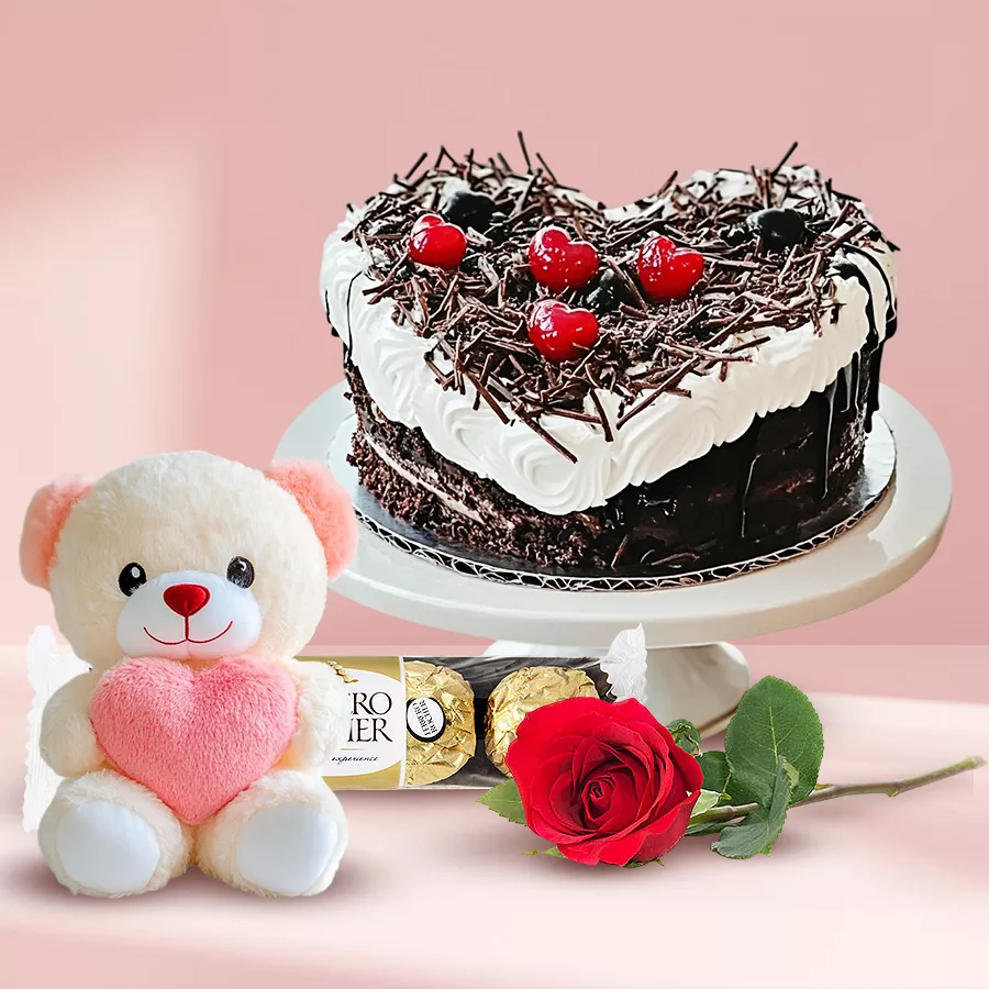 Enchanted love gift set featuring a heart-shaped Black Forest cake, red rose, teddy bear, and Ferrero Rocher chocolates.