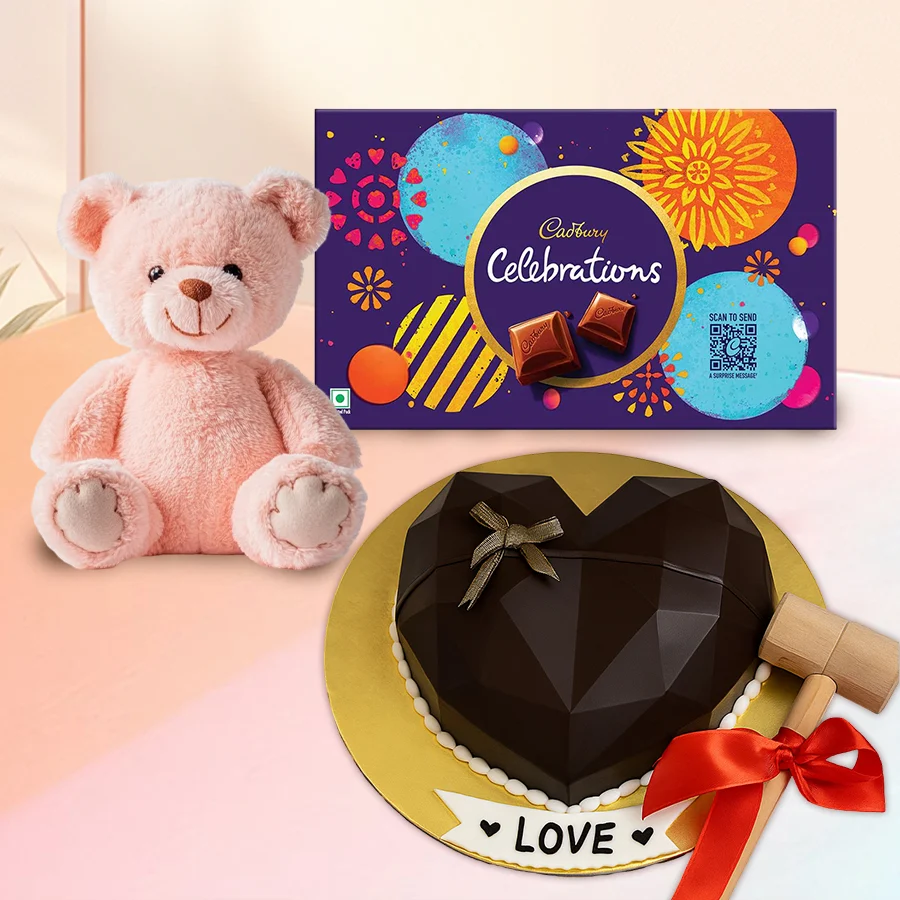 Heart-shaped piñata cake with hammer, Cadbury chocolates, and a teddy bear for celebrations.