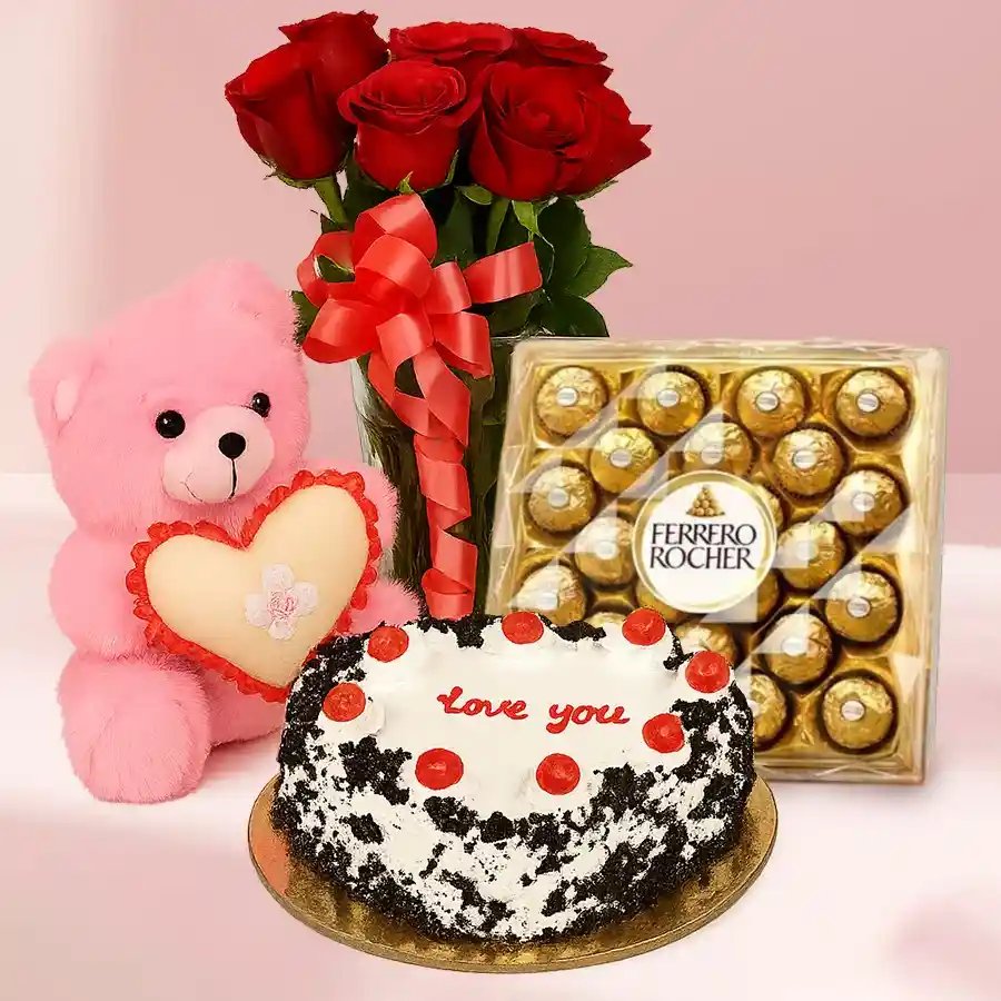 Heartfelt gift set featuring red roses, a heart-shaped Black Forest cake, a pink teddy bear, and Ferrero Rocher chocolates in a glass vase.