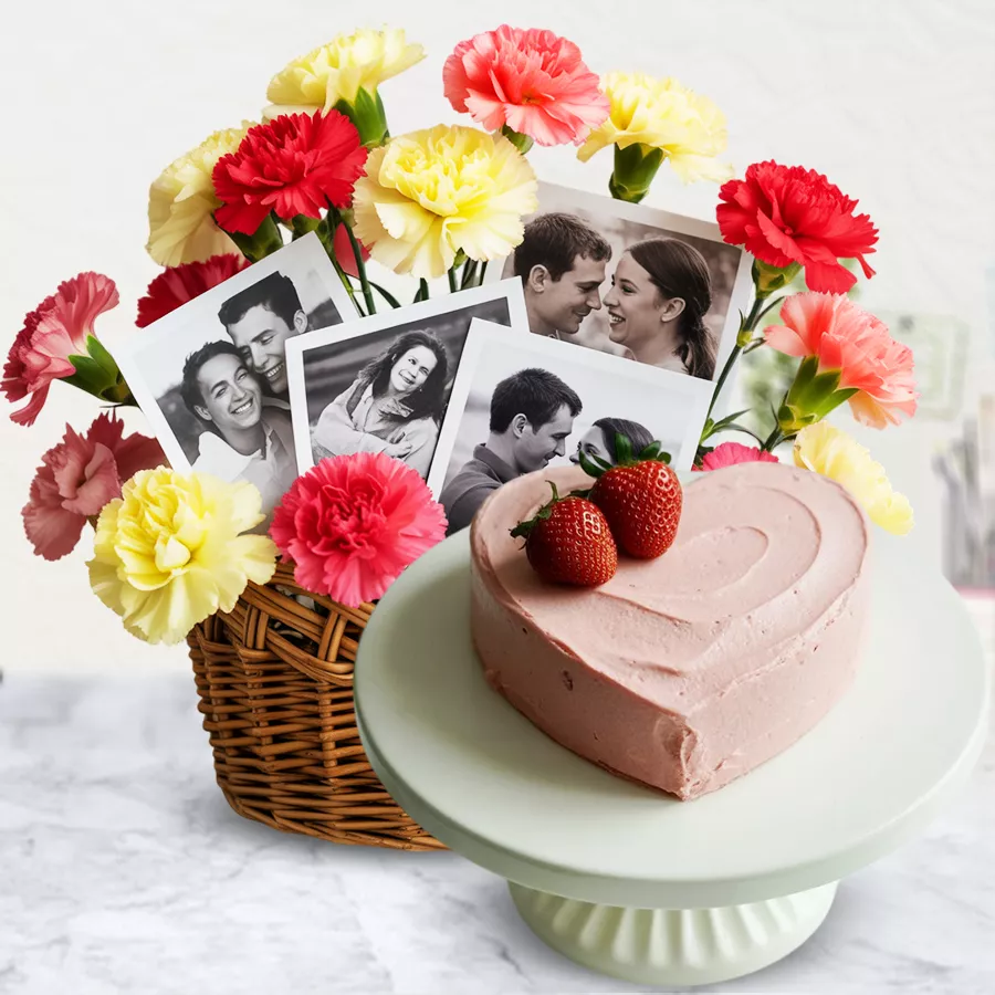 Heartfelt floral arrangement of red and yellow carnations with personalized photos and a heart-shaped strawberry cake in a basket.