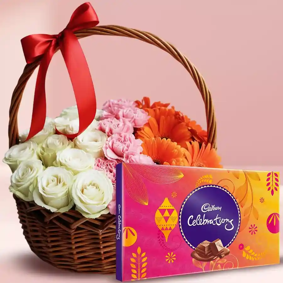 A vibrant mixed flower basket featuring white roses, pink carnations, and orange gerberas, accompanied by a Cadbury Celebrations chocolate pack.