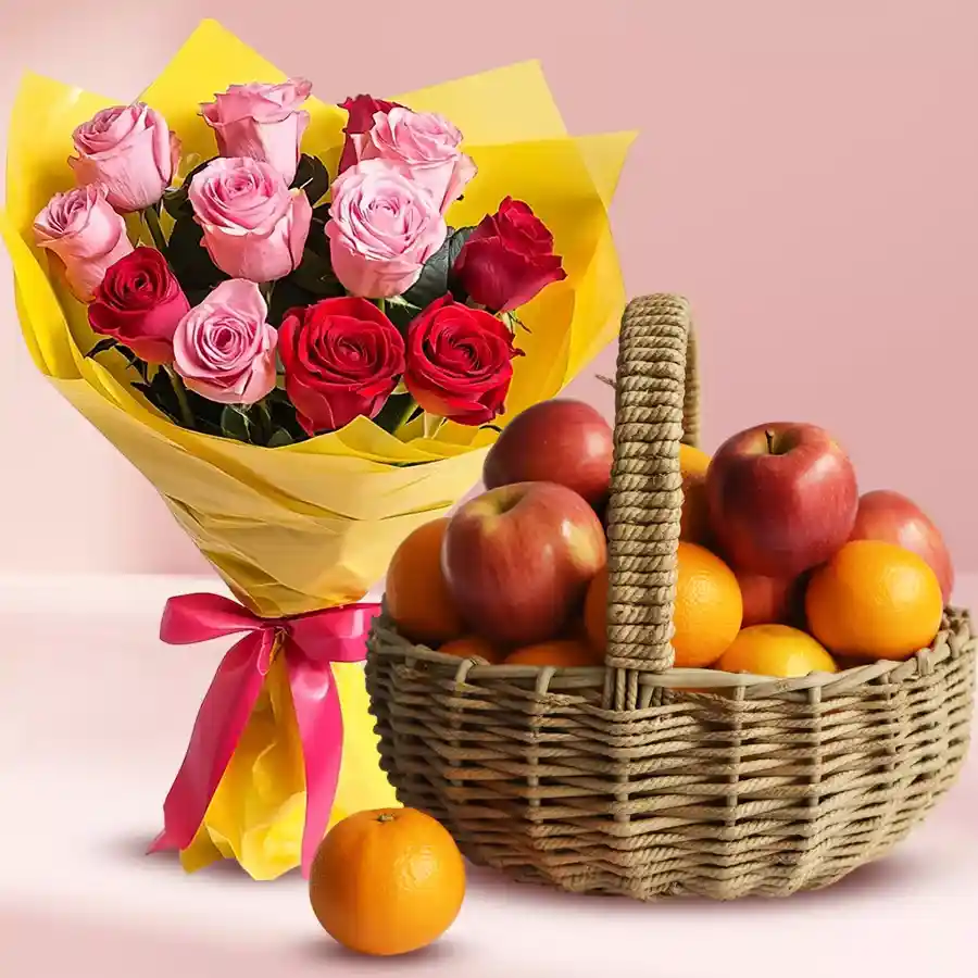 A bouquet of pink and red roses with a basket of apples and oranges.