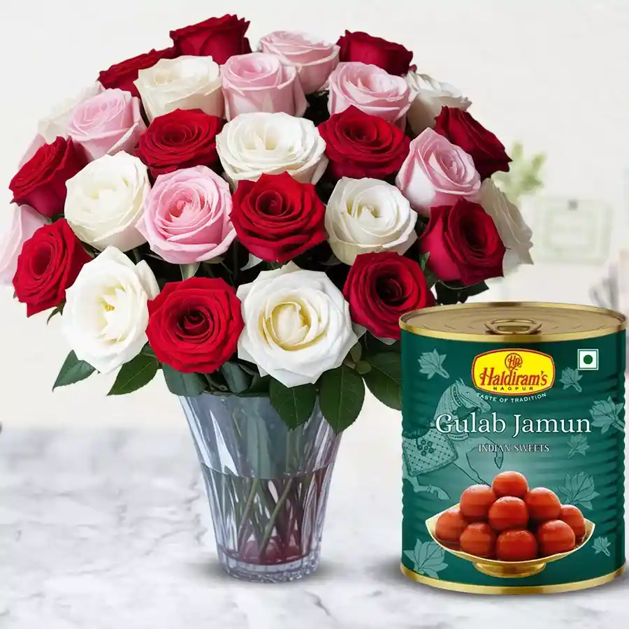 A vibrant combo of mixed roses in a glass vase alongside a tin of Haldiram Gulab Jamun.