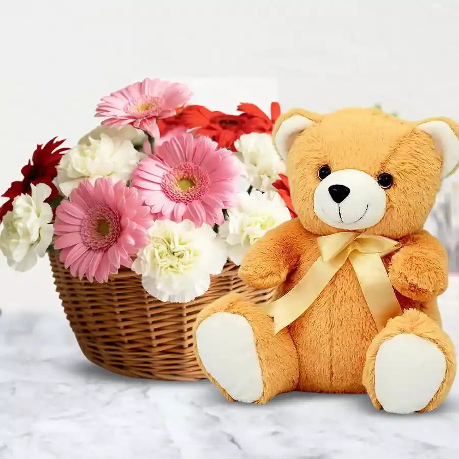 A colorful basket featuring mixed carnations and gerberas, accompanied by a cute 10-inch brown teddy bear.
