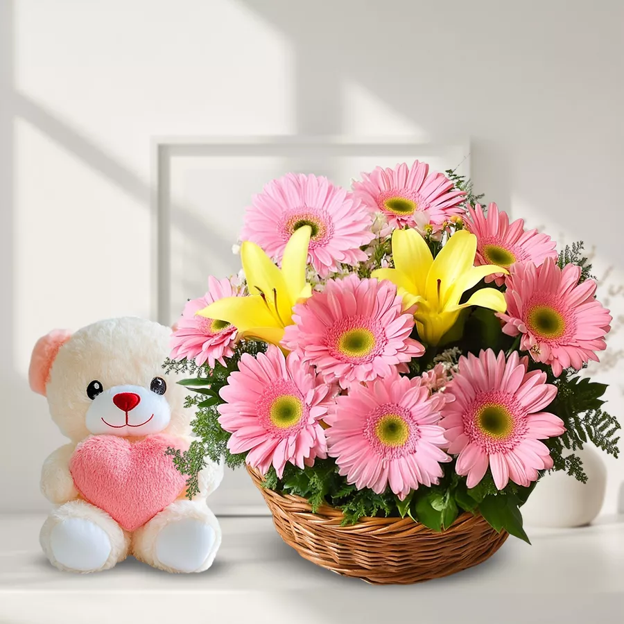 Cheerful basket arrangement of pink gerberas, yellow lilies, and a teddy bear.