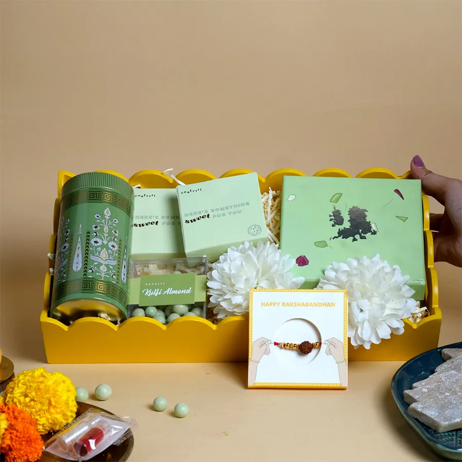 Divine Rakhi & Flavors Celebration Combo featuring a Rudraksha Rakhi, assorted sweets, nuts, cookies, and an elegant yellow tray.