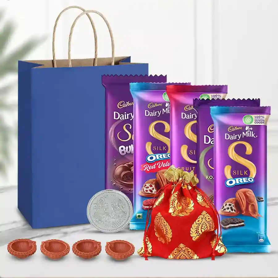 Exclusive Chocos and Dry Fruits Gift Hamper featuring Cadbury Dairy Milk Silk chocolates, cashews, raisins, decorative mud diyas, and a silver-plated Ganesh Lakshmi coin in an elegant gift bag.