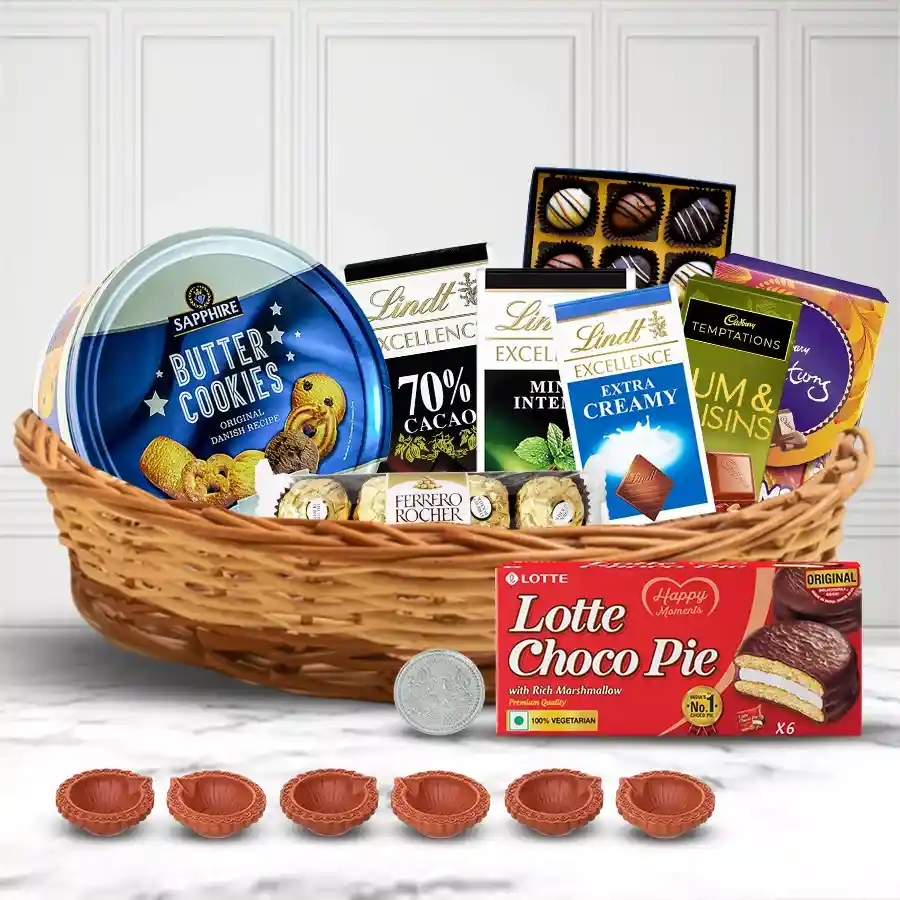 Delightful Chocolates Gift Basket for Diwali featuring premium chocolates, cookies, decorative mud diyas, and a silver-plated Ganesh Laxmi coin, arranged in a reusable cane basket.