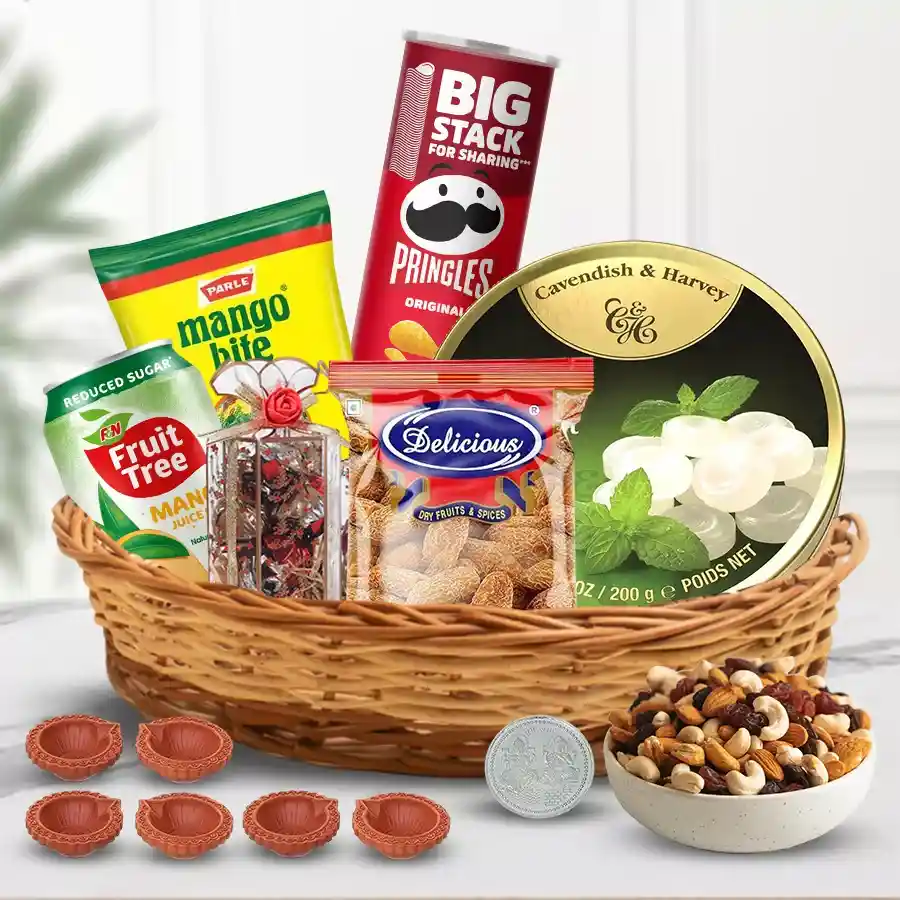 Amusing Assortments Gift Hamper for Diwali featuring sweet dates, mango toffees, handcrafted chocolates, mint candies, mango juice, Pringles, dry fruits, decorative mud diyas, and a silver-plated Ganesh Lakshmi coin in a reusable cane basket