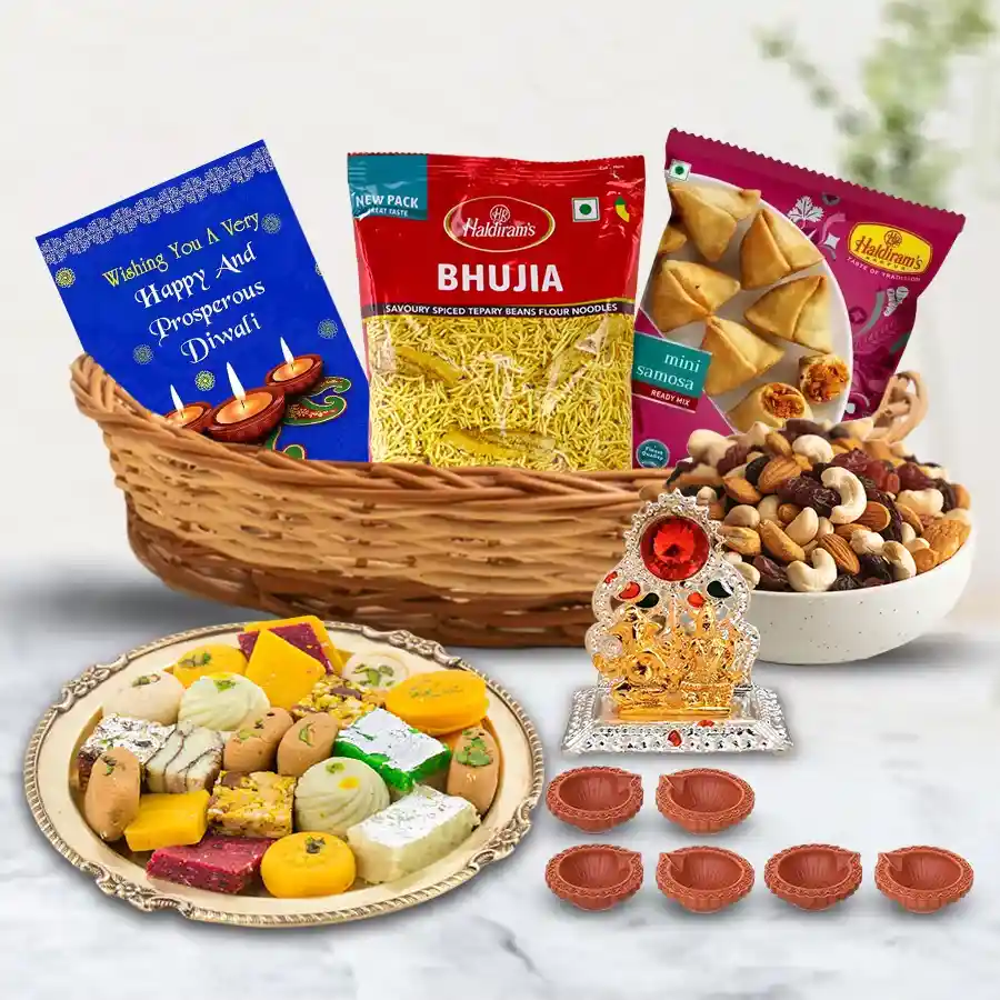 Marvelous Sweets N Savory Gift Hamper featuring assorted dry fruits, Haldiram sweets, Bhujia, mini samosas, Antique Ganesh Laxmi Mandap, decorative mud diyas, and a silver-plated Laxmi Ganesh coin in a cane basket with a Diwali greetings card.