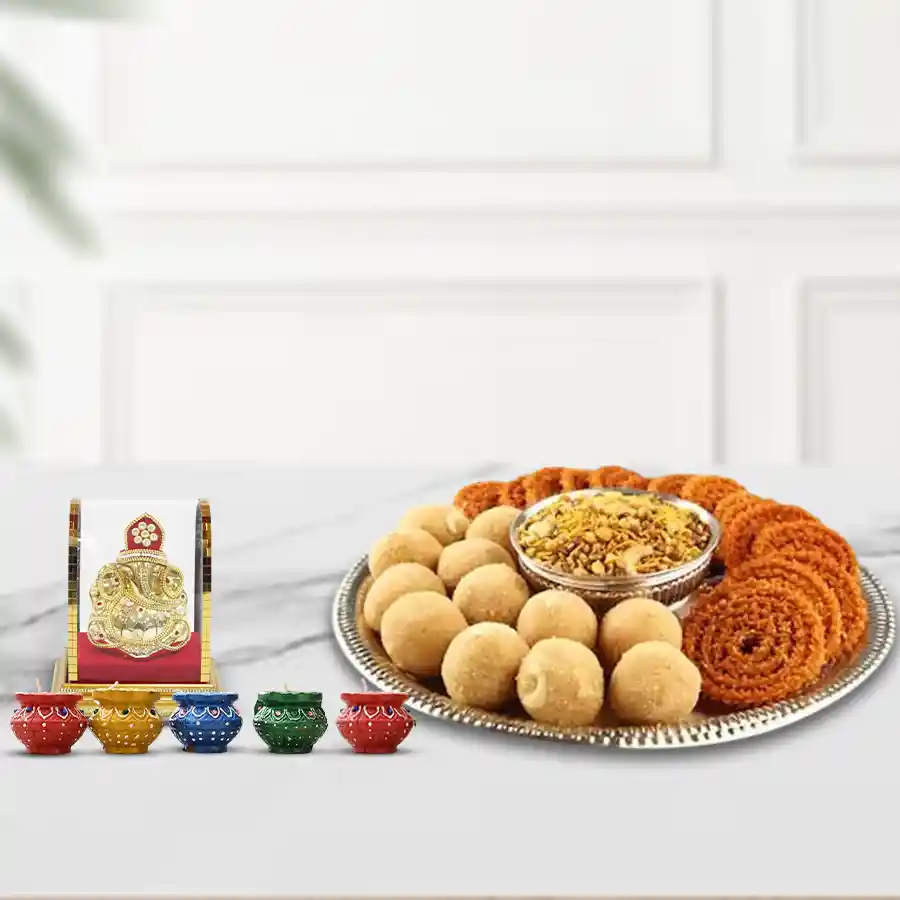 Exclusive Diwali sweets and savory platter featuring besan ladoos, muruku, bhikharam mixture, silver-plated pooja thali, bowl, ganesh idol, and diyas.