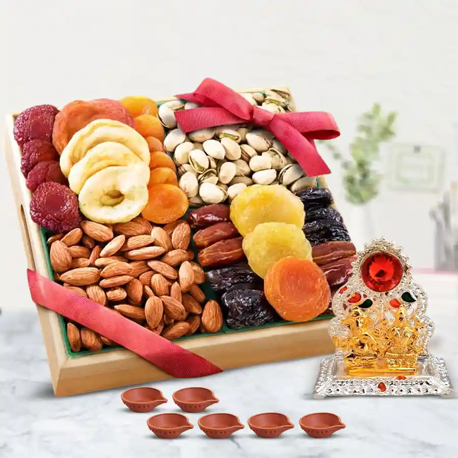 A wooden tray filled with a variety of dry fruits including almonds, pistachios, apricots, dates, strawberries, and cranberries, adorned with a red ribbon, accompanied by a Ganesh Lakshmi Mandap and six decorative diyas.