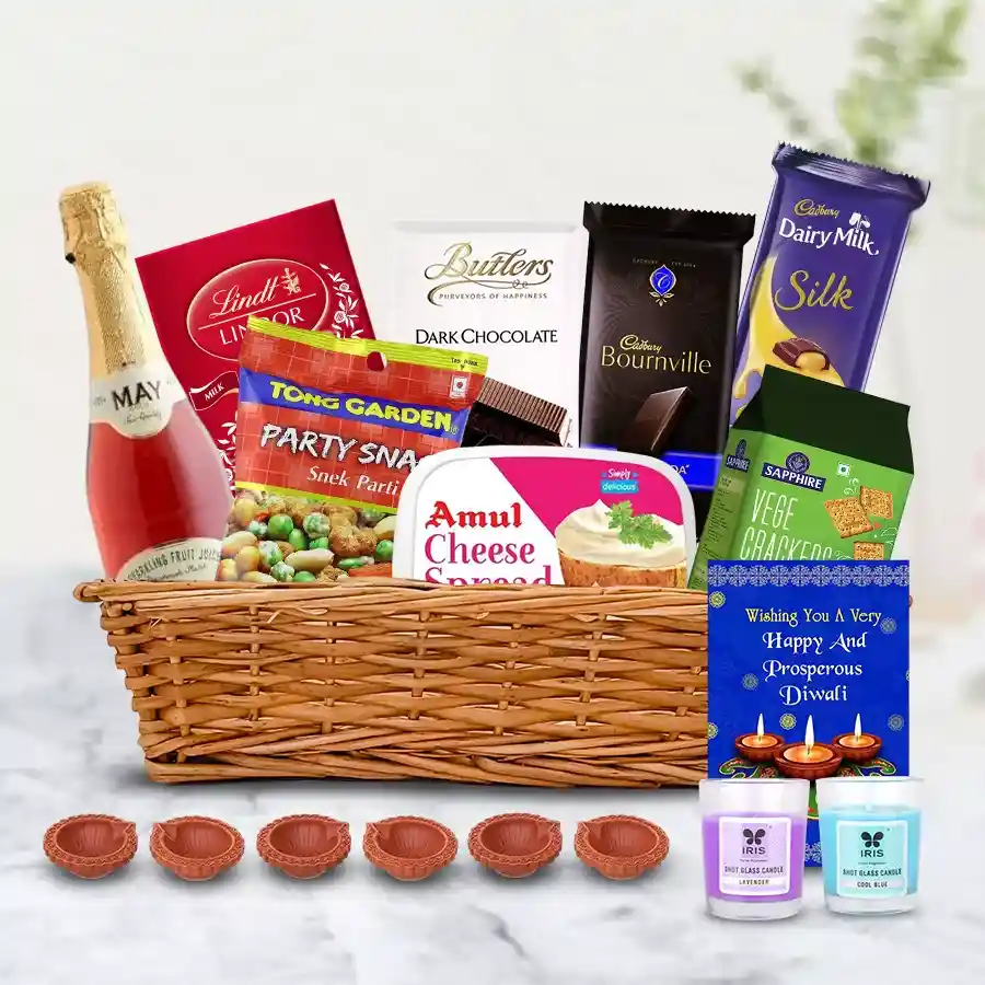 Marvelous Assortments Gift Hamper for Diwali featuring fruit juice, snacks, cheese spreads, chocolates, diyas, aroma candles, and a greeting card in a chic cane basket.