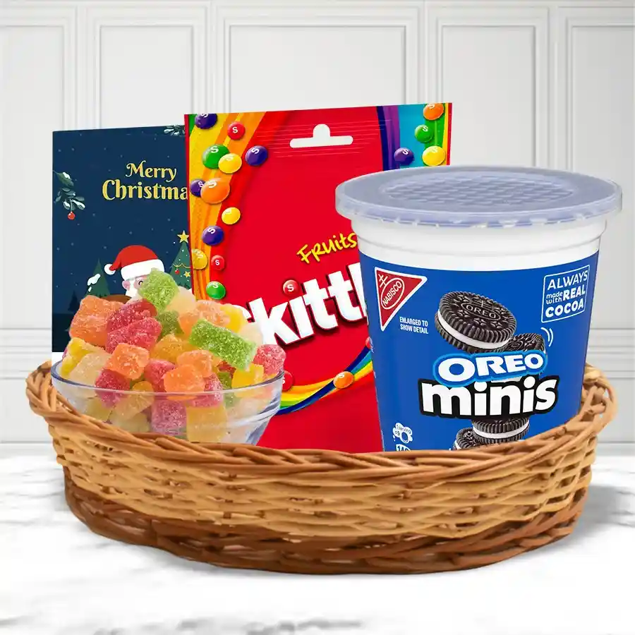 A festive cane basket filled with colorful Skittles Fruits Chocolates, Cadbury Mini Oreos, and assorted fruit jellies, topped with a cheerful Christmas card.