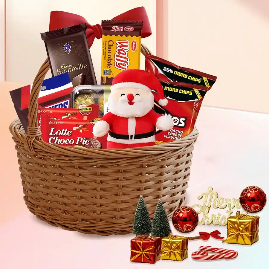 A beautifully arranged gift basket filled with assorted chocolates, snacks, and festive decorations, including a Santa Claus soft toy and a red bow.