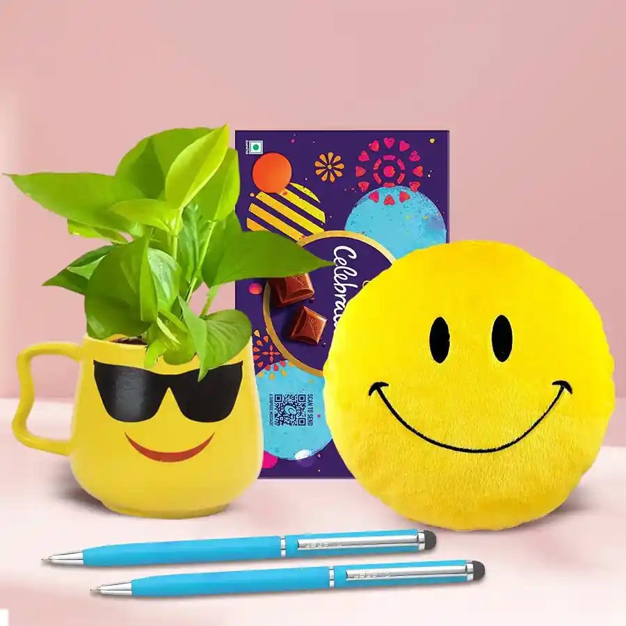 Exotic Plants Gift Hamper featuring a Money Plant in a Smiley Cup, a Smiley Cushion, two ballpoint pens, and a Cadbury Celebration chocolate bar