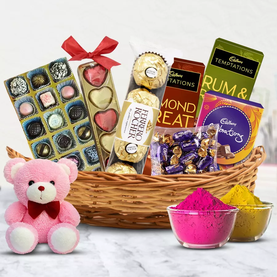 Ambrosial Chocos Gift Basket for Holi featuring homemade and premium chocolates, heart-shaped treats, Ferrero Rocher, Cadbury chocolates, a 6-inch teddy, and multicolor herbal gulal in a charming cane basket