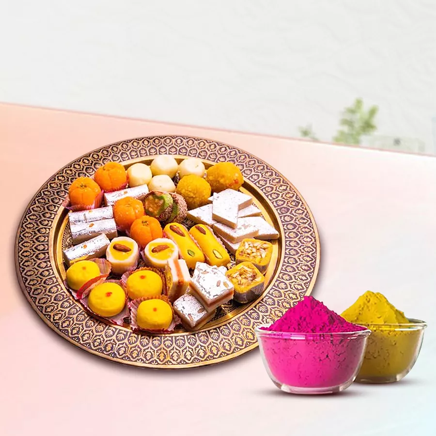 A beautifully arranged assortment of Indian sweets including Kaju Barfi, Kesar Peda, Desi Ghee Laddoos, and Mawa Gilori, presented in an elegant box, accompanied by two packets of organic herbal Gulal.