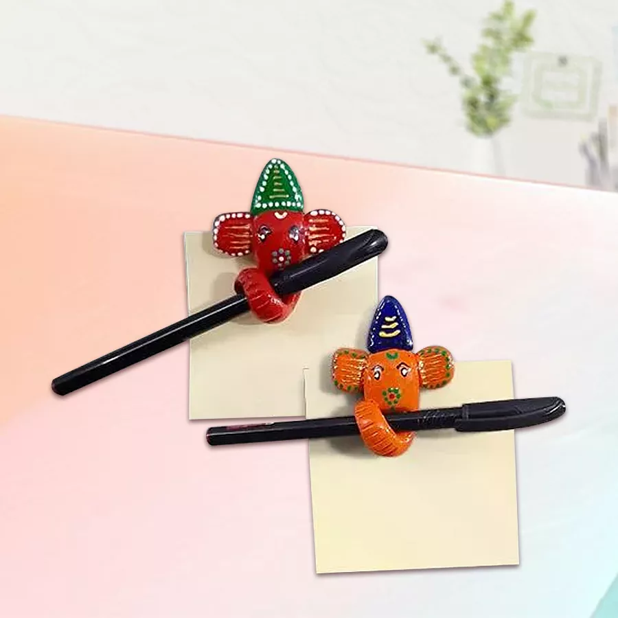Handmade Ganesha pen holder fridge magnet with two ball pens and sticky notes on a desk