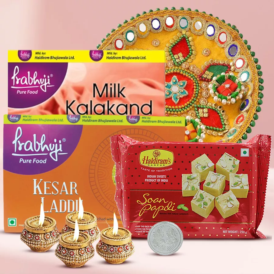 Ambrosial Haldiram Gift Hamper featuring Milk Kalakand, Kesaar Laddu, Soan Papdi, Designer Steel Thali, terracotta Diyas, and Laxmi Ganesh Silver Plated Coin for Diwali celebrations.