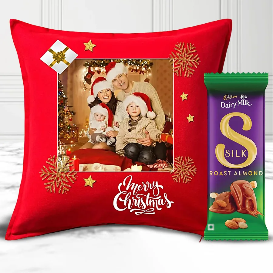 Personalized pink Merry Christmas fur cushion with a heart shape and a Cadbury Dairy Milk Silk Roast Almond Chocolate Bar on a festive background.