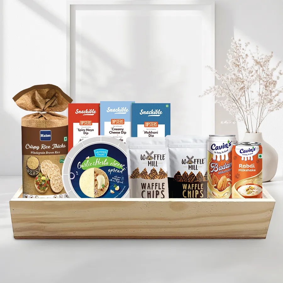 Breakfast hamper featuring organic brown rice cakes, cheese spread, dips with ragi and soya chips, chocolaty waffle chips, and milkshakes arranged on a wooden tray.