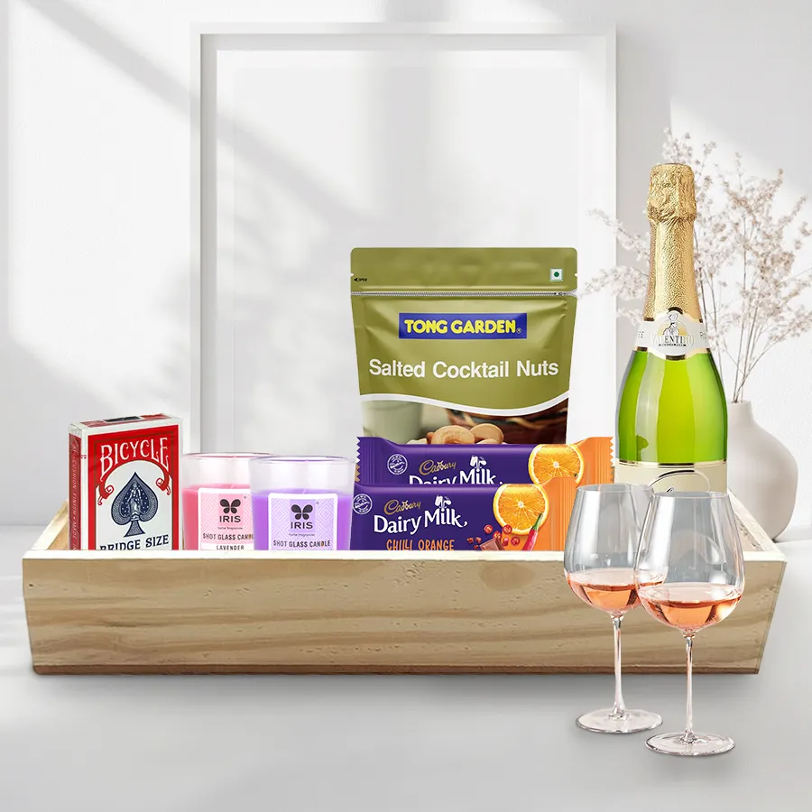 Finest Hamper of Christmas Evening Snacks featuring wine glasses, sparkling fruit wine, cocktail nuts, chocolates, playing cards, candles, and a wooden tray