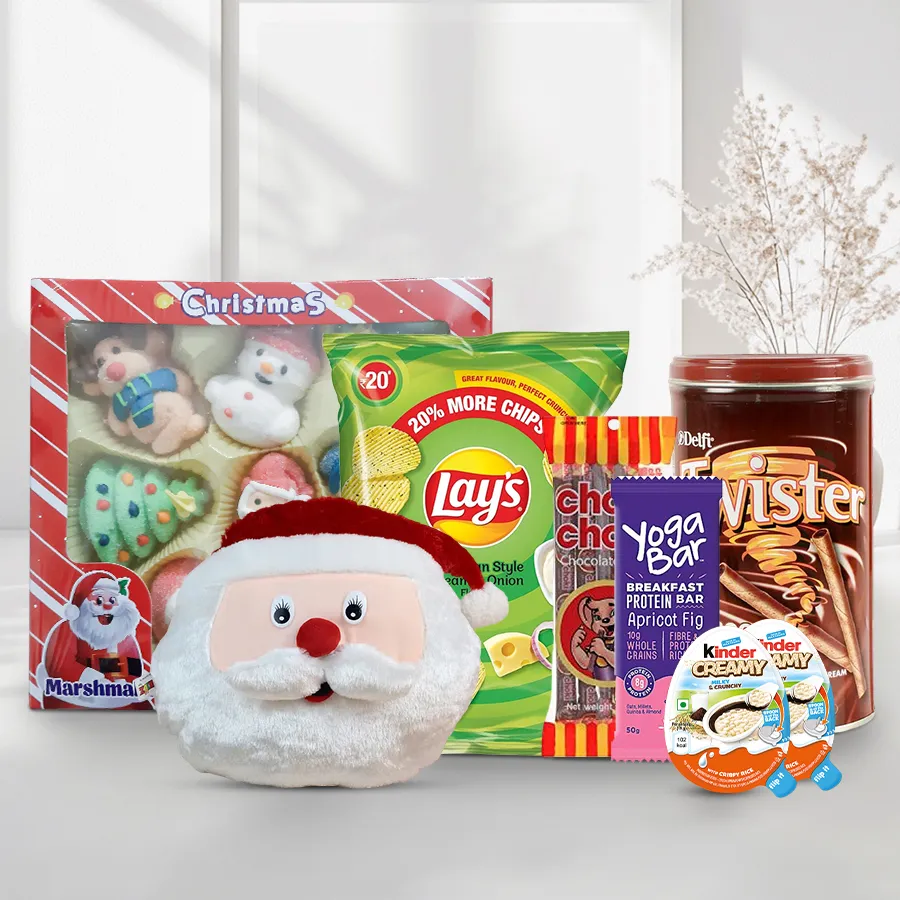Santa Claus face cushion with assorted holiday treats including protein bar, chocolate snacks, chips, wafers, and marshmallows.