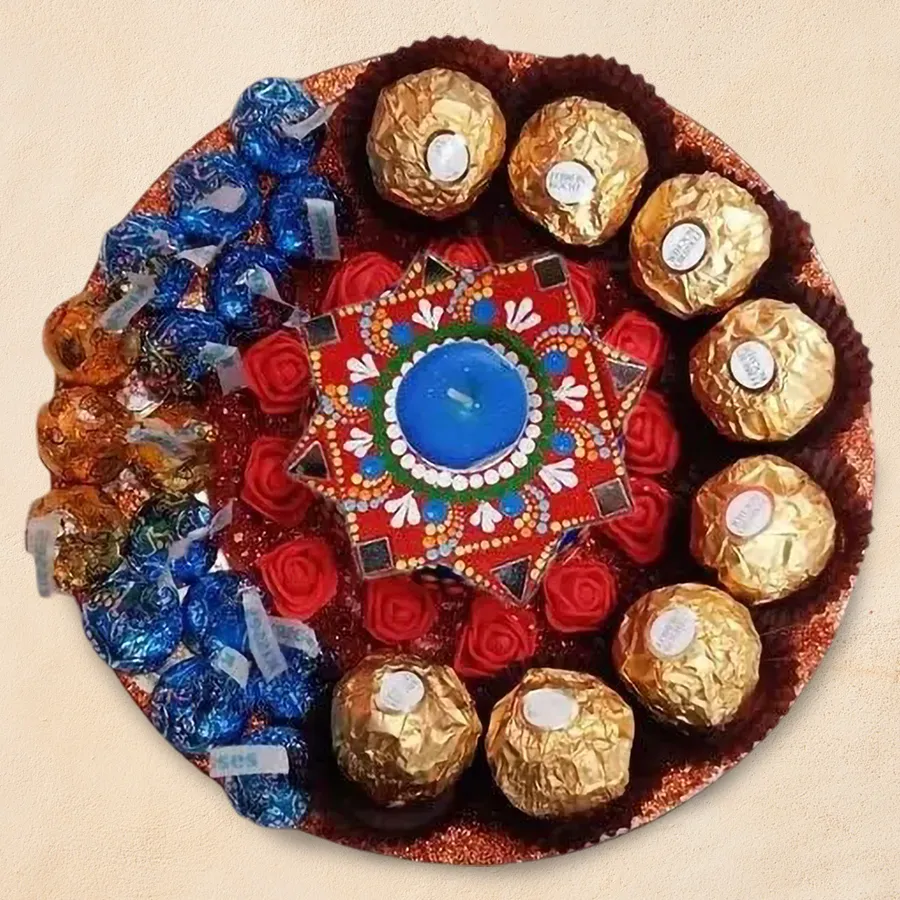 Gift plate featuring luxurious Ferrero Rocher chocolates, Hershey’s Kisses Cookie ’n Cream, a Dot Mandala Diya, and vibrant decorative flowers arranged elegantly.