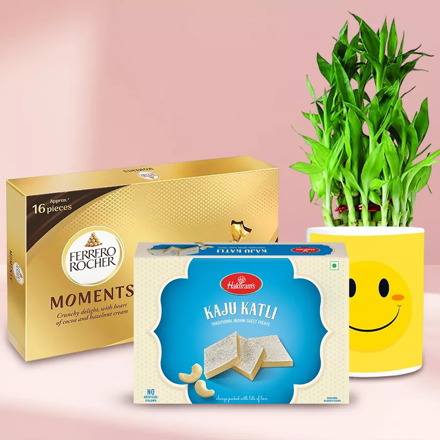 Lovely Smiley Mug with a 2-Layer Bamboo Plant, Ferrero Rocher Moments chocolates, and Kaju Katli sweets arranged as a Mother's Day gift set.