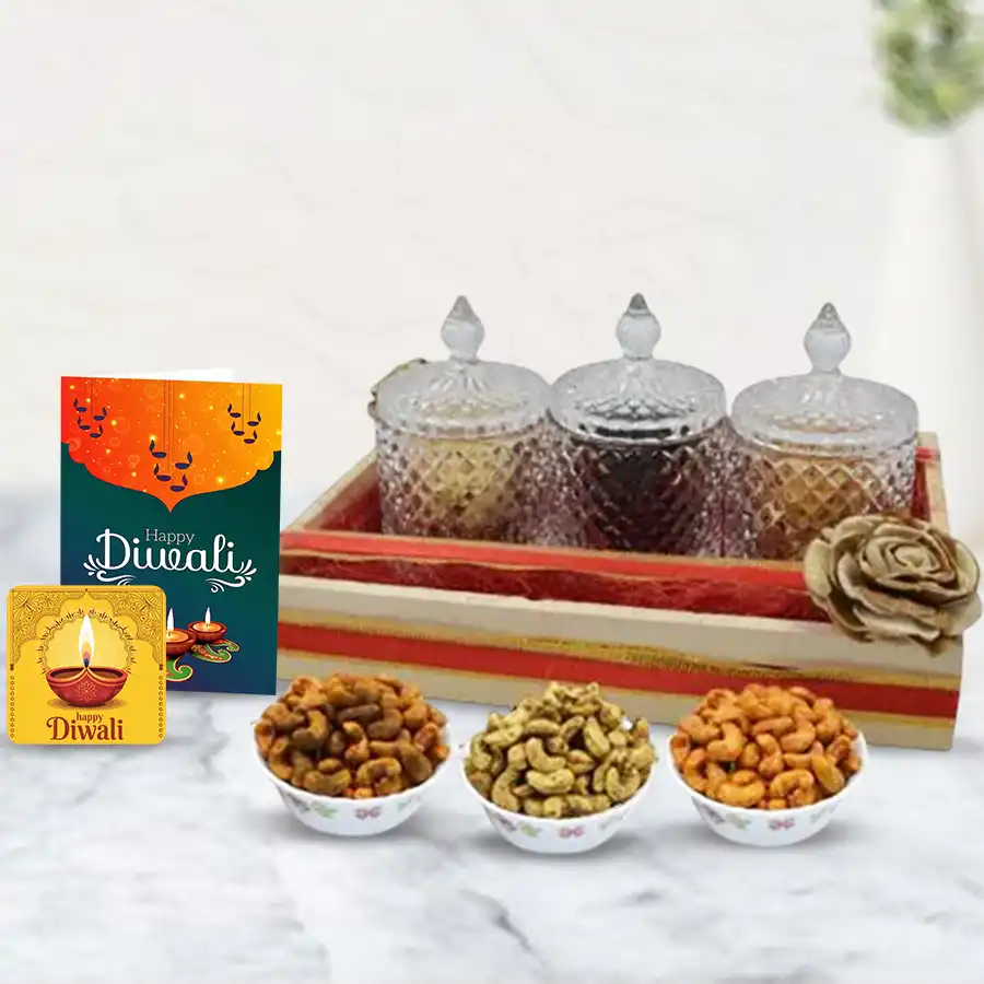 A beautifully arranged wooden tray featuring three designer glass jars filled with crunchy, masala, and cheese-flavored cashews, accompanied by a handmade Happy Diwali fridge magnet and a greeting card, all set against a festive backdrop.
