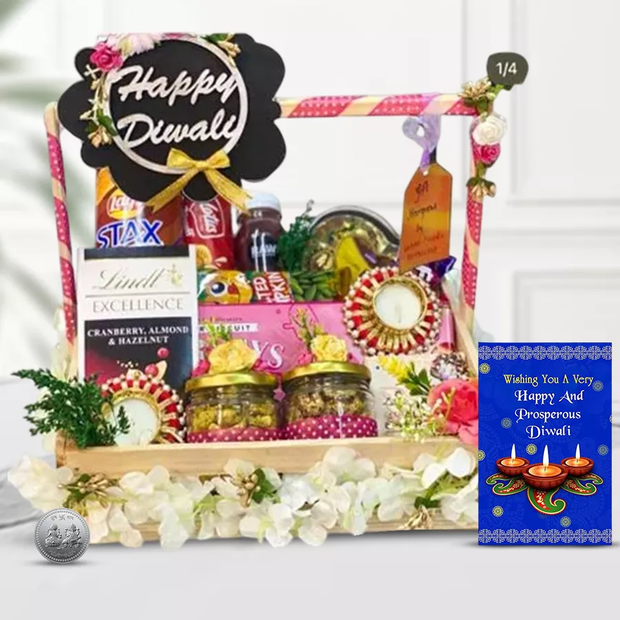 Gourmet gift hamper featuring potato chips, cookies, chocolates, juice, wafers, nuts, candle holders, and a Diwali wishing card in a reusable basket.