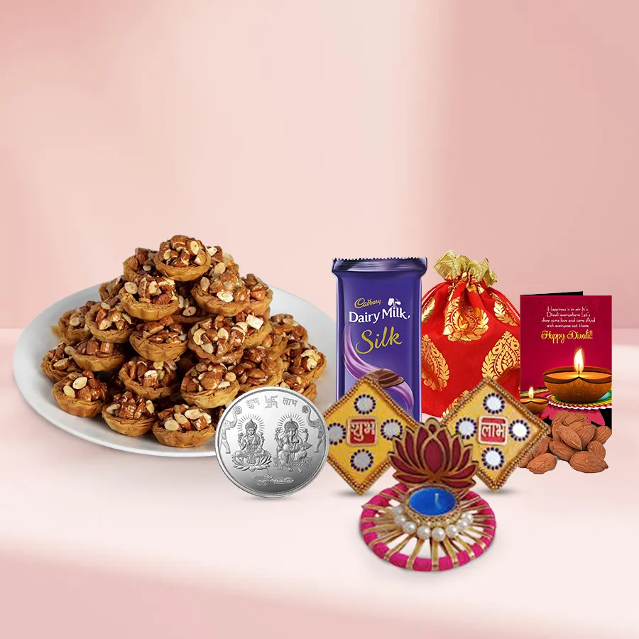 Gift basket featuring tart baklava, a Cadbury Silk chocolate bar, a potli of cashews, a silver-plated Ganesh Lakshmi coin, a Lotus tea light candle holder, a Shubh Labh wall sticker, and a Diwali card, all beautifully arranged for the festive season.