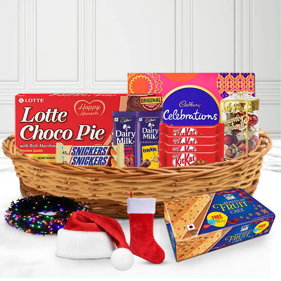 Heavenly Christmas Cake Chocolate and Décor Combo in a stylish cane basket featuring American Fruit Cake, Cadbury treats, KitKats, Snickers, Christmas decorations, twinkling lights, caps, and stockings.