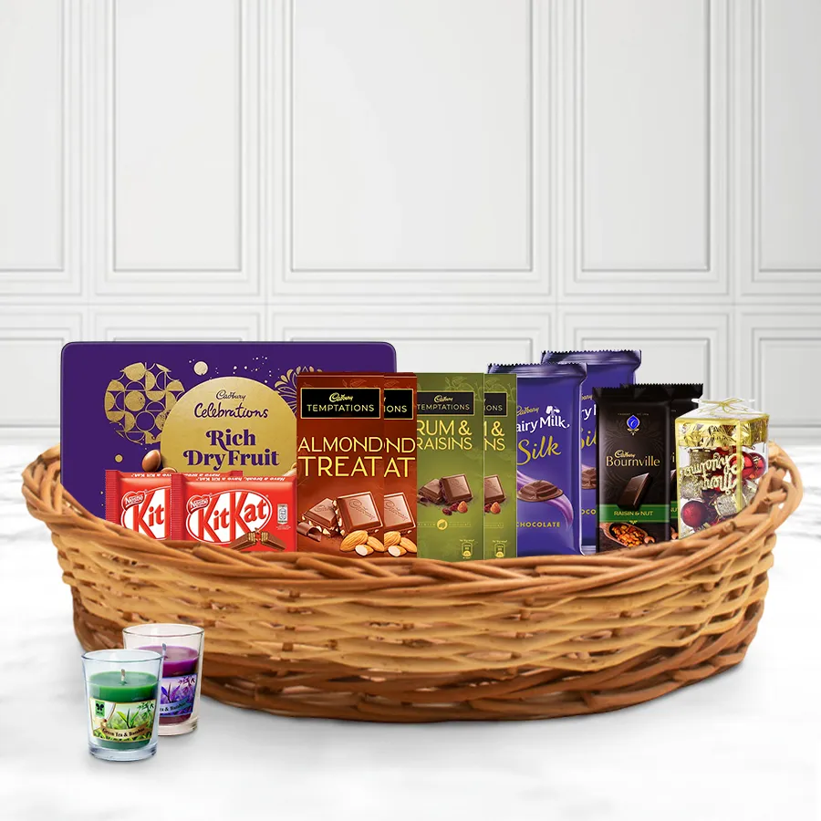 A festive Christmas basket filled with Cadbury chocolates, Nestle Kit Kats, a dry fruit tin, an Aroma candle, and decorative elements, all arranged in a stylish reusable basket.
