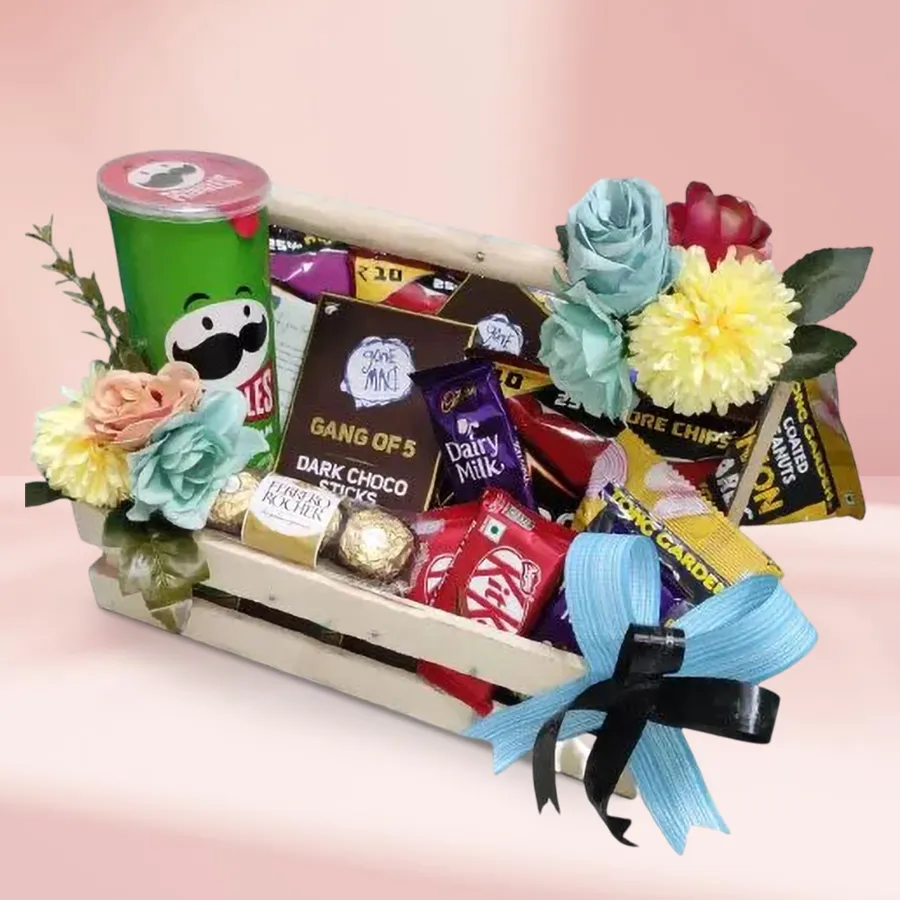 Sumptuous gift tray filled with snacks and chocolates including peanuts, nachos, chips, chocolate sticks, KitKat and Dairy Milk bars, arranged on a wooden tray.