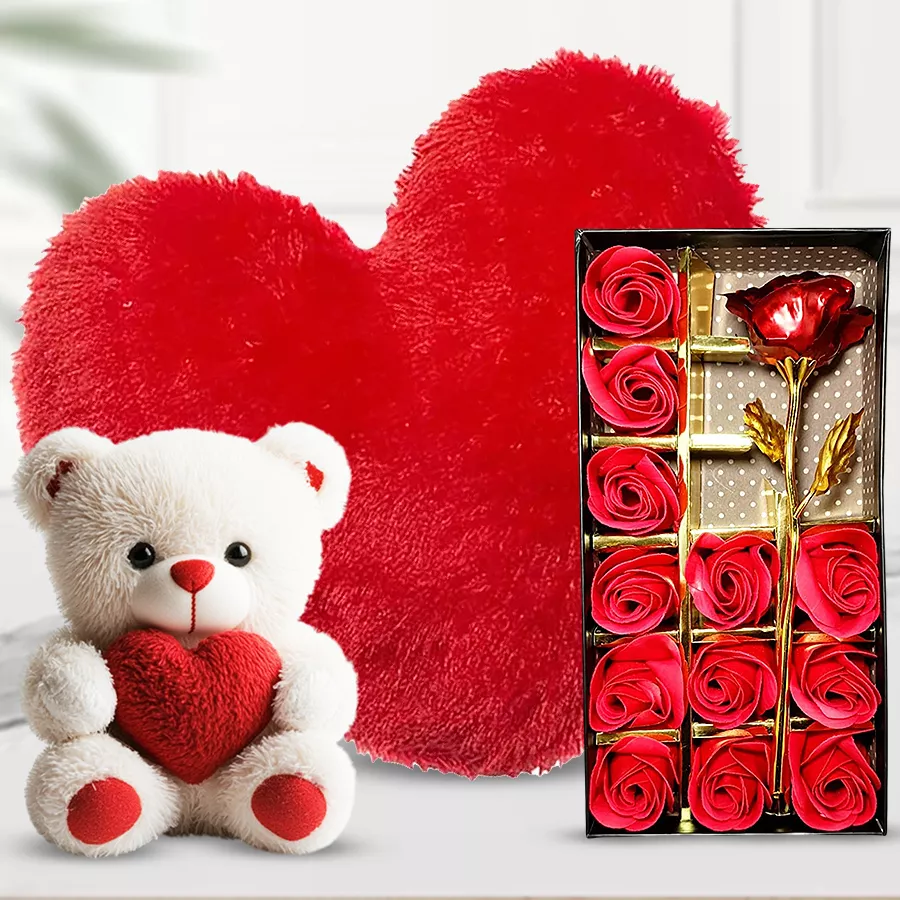 Teddy bear holding a heart, red roses in an elegant box, and a heart-shaped cushion arranged together as a gift set.