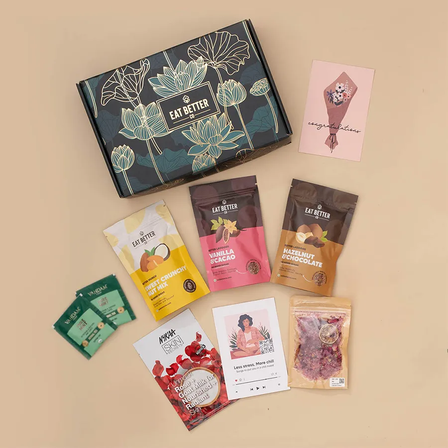 Premium Goodness Treat Hamper in Midnight Lotus Gift Box featuring laddoos, nut mix, herbal teas, foot salts, and face masks, beautifully presented with gold foil accents.