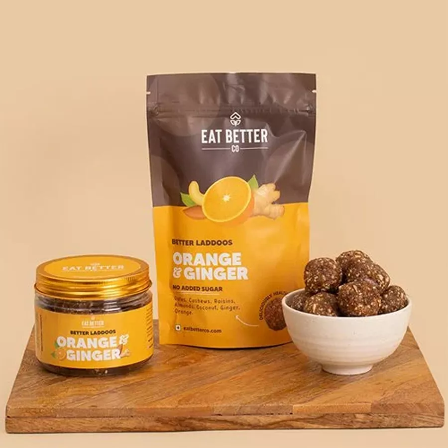 Premium Sugar Free Orange and Ginger Laddoos arranged on a wooden platter with nuts and oranges in the background.