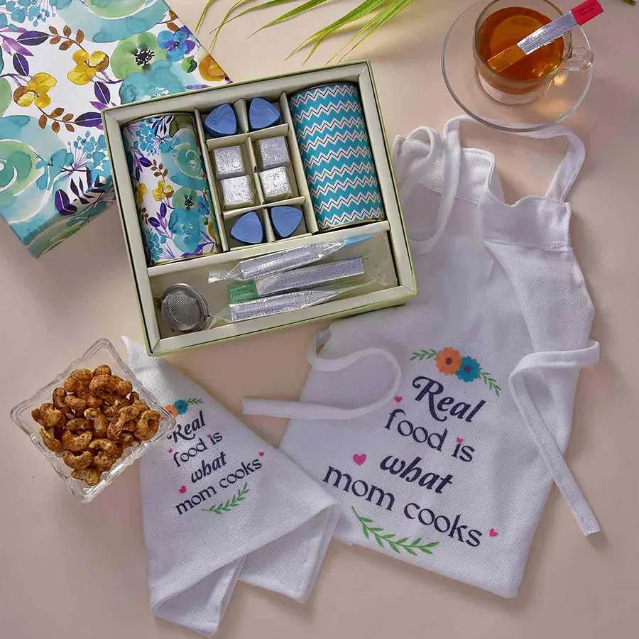 BeauTeaful Tea Treat Gift Hamper for Mom featuring a MOM apron, hand cloth, rose tea, masala kaju, chocolates, tea bags, and a stainless steel tea filter.