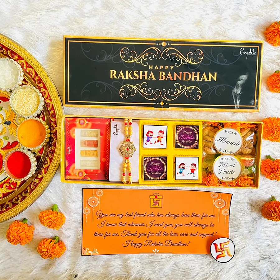 Beautiful Pearl and Metal Rakhi with assorted treats including chocolates, almonds, mixed fruits, Roli Tikka, and a greeting card in a printed box.