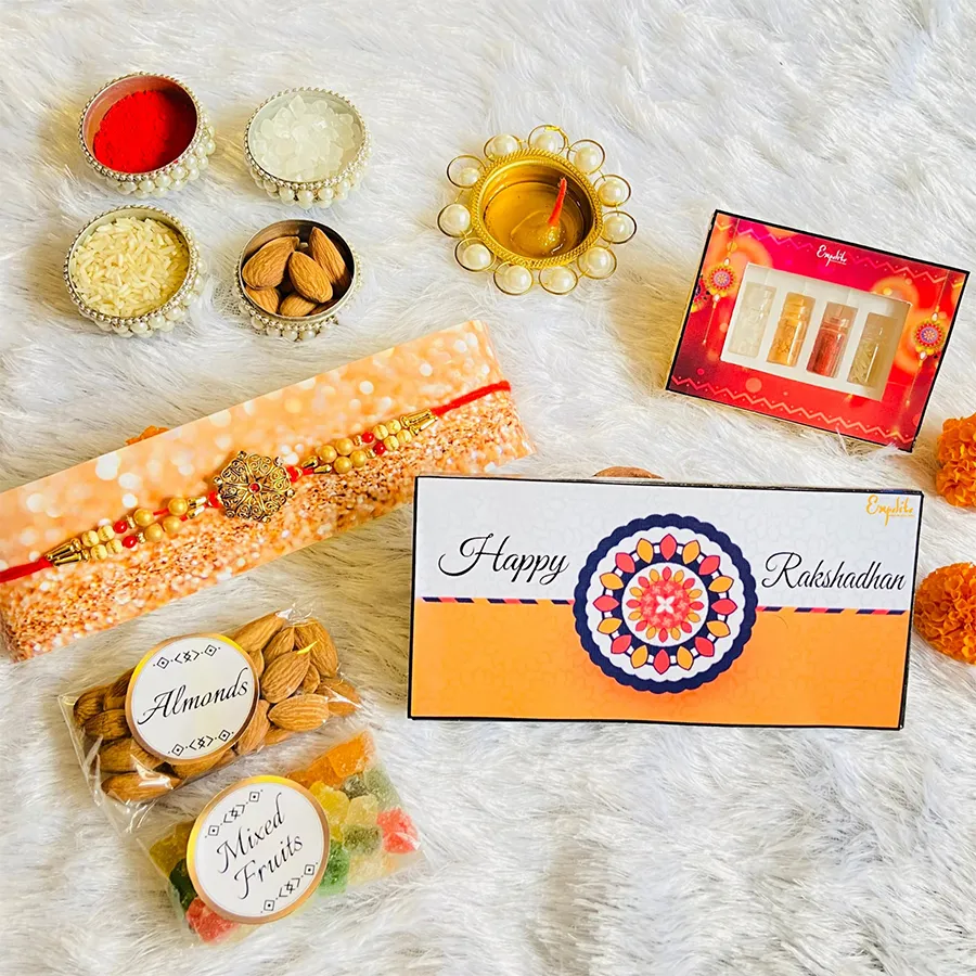Rakhi Gifts hamper featuring a colorful I Love My Brother Rakhi, handcrafted chocolates with dryfruit and cranberry fillings, crunchy almonds, mixed fruits, Roli Tikka, Chandan, Chawal, Mishri, and a Rakhi greeting card in a themed box.