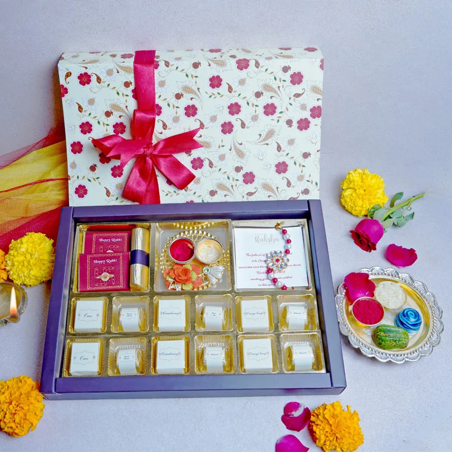 Sibling Bond Sweets hamper featuring two milk chocolate bars, an orange crisp log, a kumkum thali, twelve assorted chocolates in six flavors, a designer rakhi, and a greeting card.