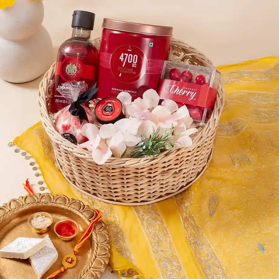 Delight Hampers for Brothers featuring popcorn, cherry dragees, shower gel, lip balm, bath bomb, flower arrangement, reusable round basket, and Meenakari Rakhi