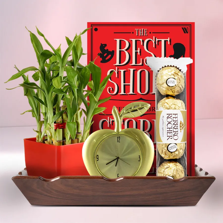 Retirement gift hamper featuring a book, Ferrero Rocher chocolates, a golden apple-shaped table clock, and a lucky bamboo plant in a wooden tray