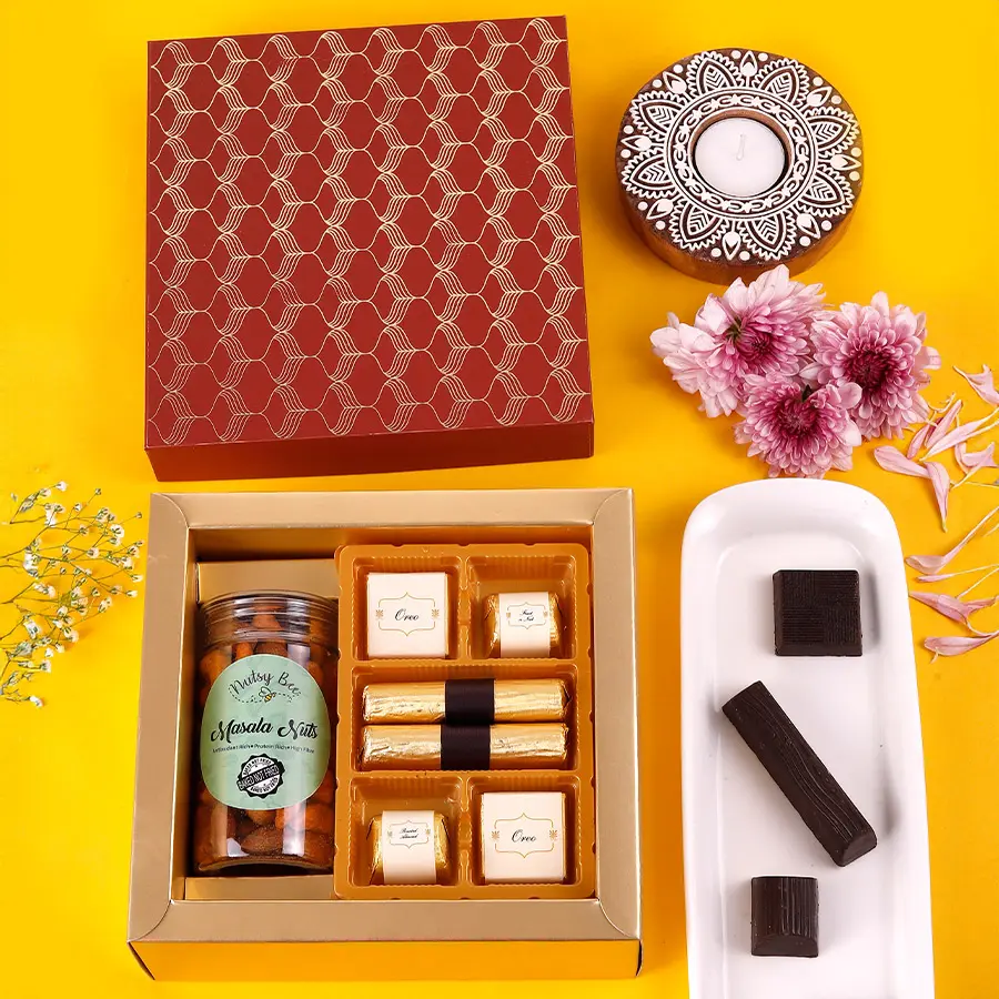 A beautifully arranged box of gourmet treats including crunchy masala nuts, assorted chocolates, and granola chocolate logs, showcasing vibrant colors and textures.
