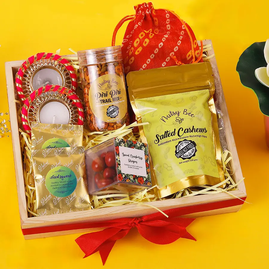 A festive hamper filled with assorted chocolates, piri piri trail mix, cranberry dragees, salted cashews, and two decorative diyas.